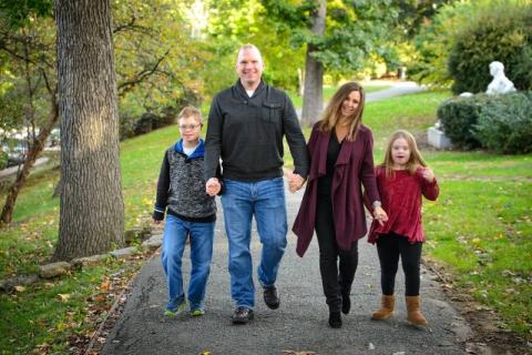 A photo of a family with a dad, two tween kids, and a mom walking hand in hand outdoors.]