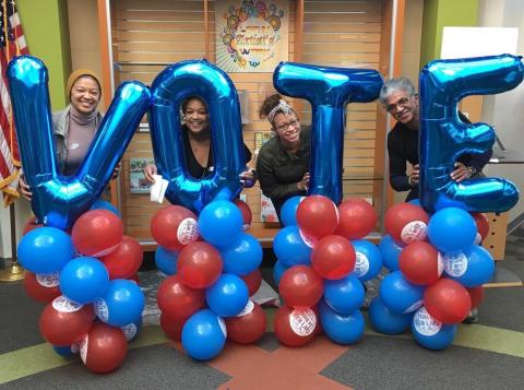 Four smiling MomsRising Volunteers hold up balloons that spell VOTE. 