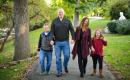 A photo of a family with a dad, two tween kids, and a mom walking hand in hand outdoors.]