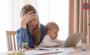 A stressed out mom with blond hair hold her baby in front of a stack of bills