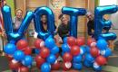 Four smiling MomsRising Volunteers hold up balloons that spell VOTE. 